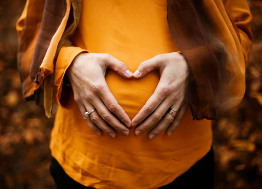woman with hands forming heart on pregnant belly